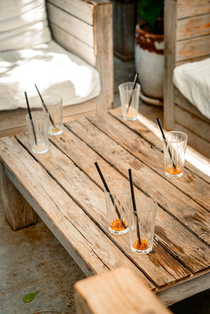 Empty glasses with straws on a rustic wooden table in outdoor seating area.